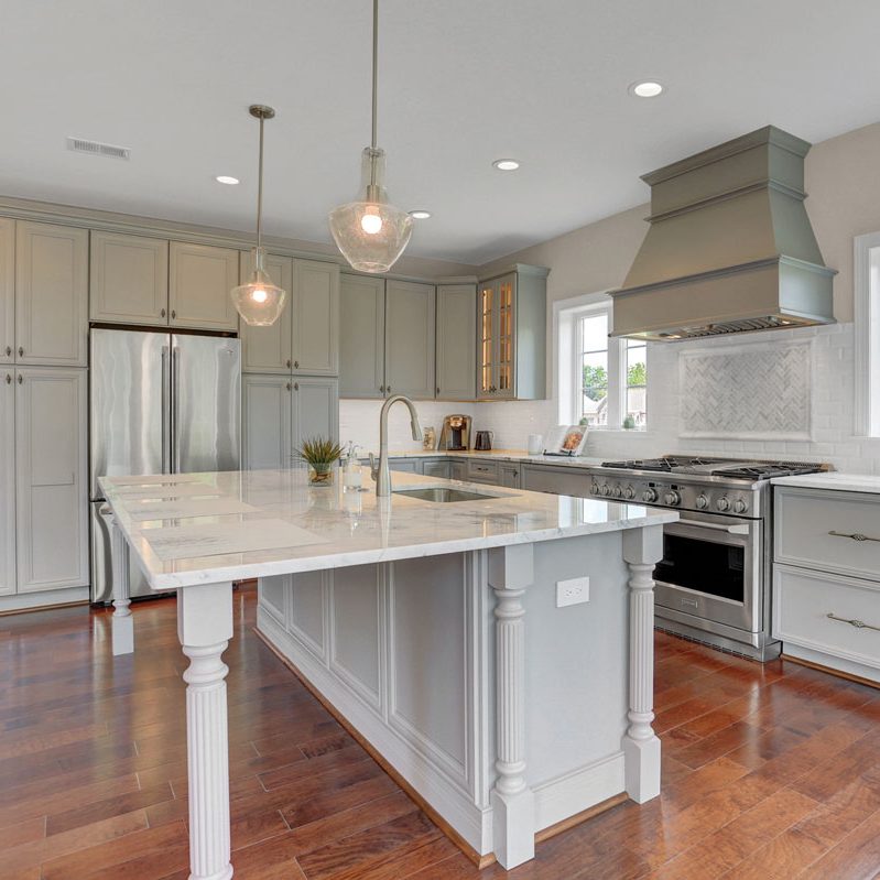 Kitchen with sage cabinetry and a white wood island with a marble countertop