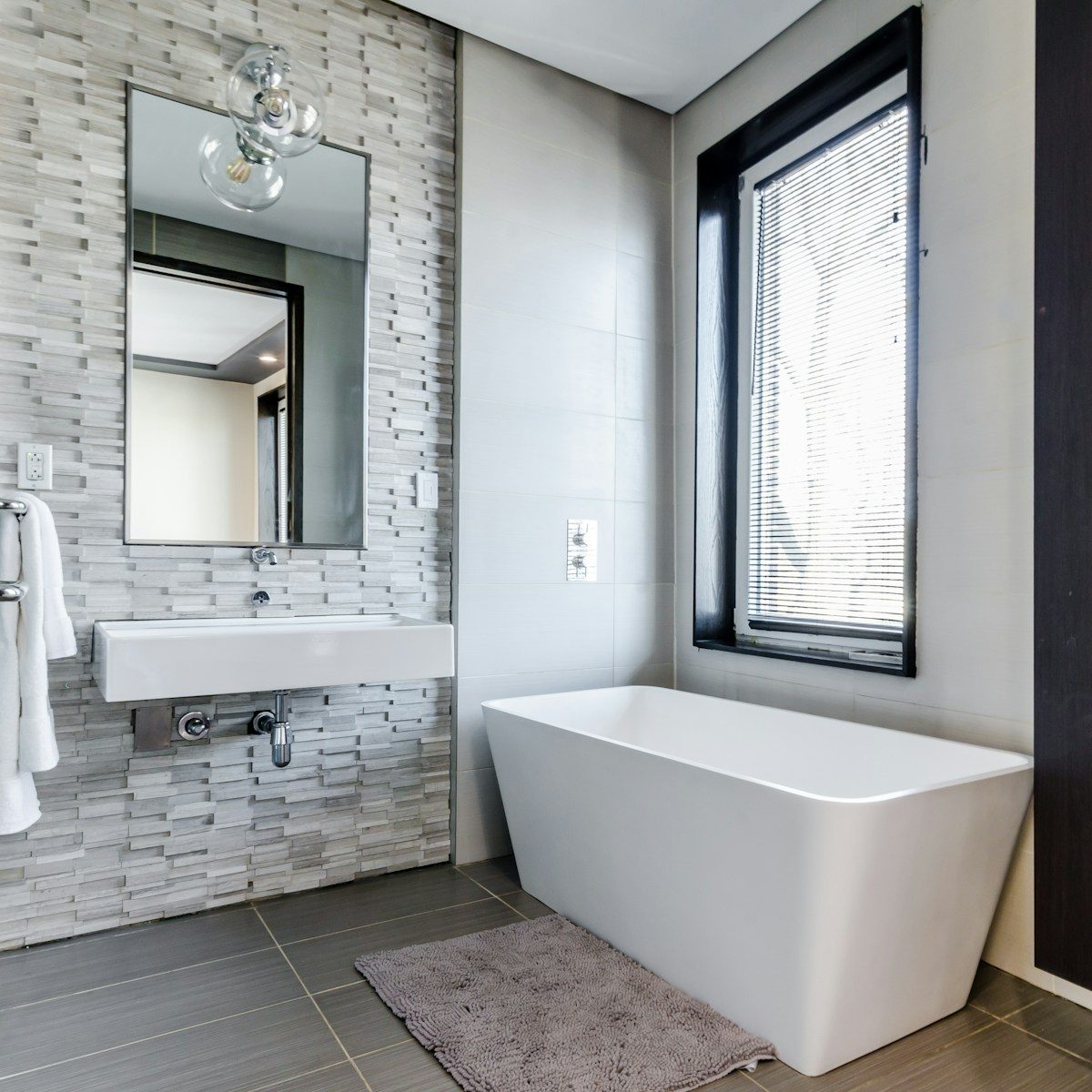 Bathroom with contrasting grey tile accent walls, white ceramic sink and white ceramic tub with window view