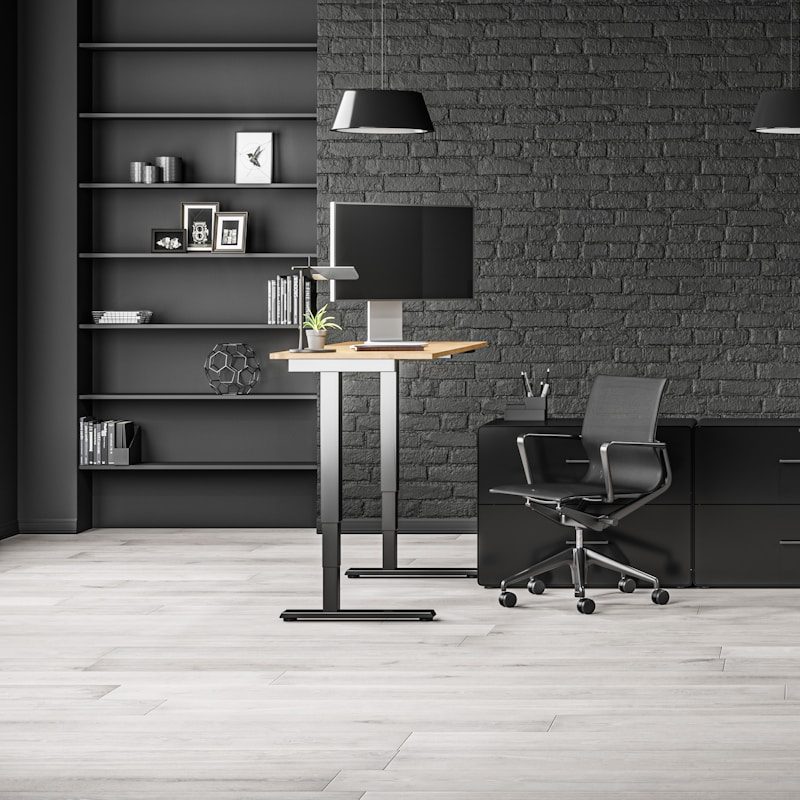 Home workspace with standing desk, computer chair, black shelves and black exposed brick walls