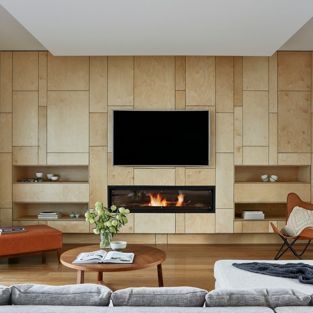 Living room with grey couch, coffee table, wooden wall with built-in tv and electric fireplace