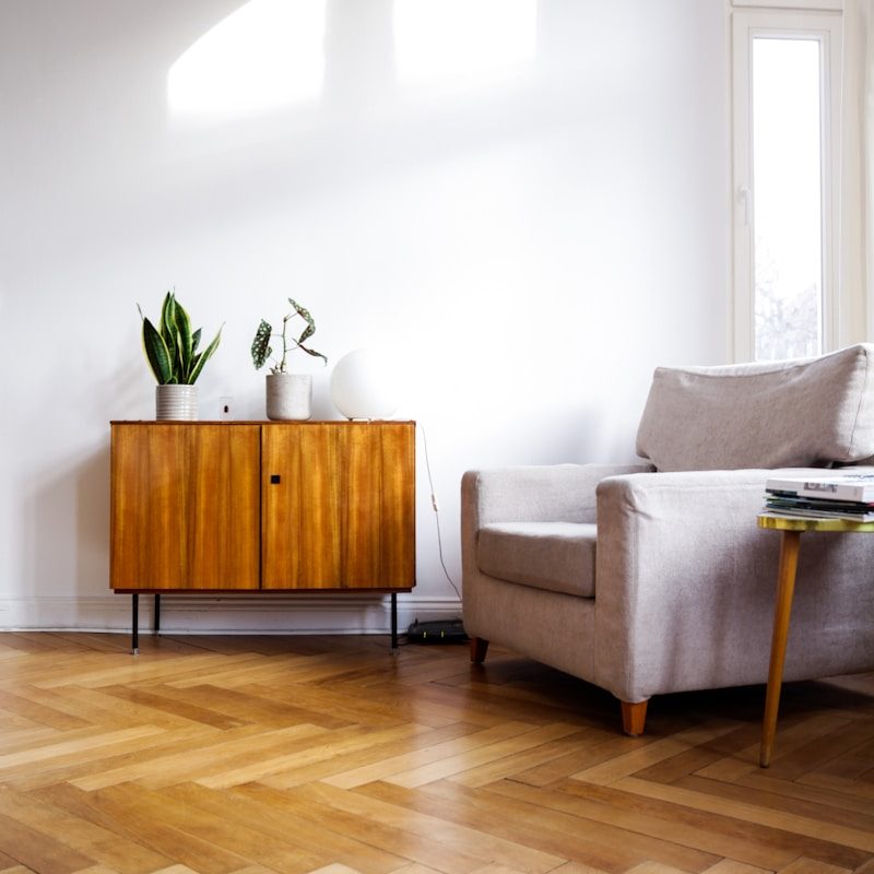 Reading nook with chevron wood flooring, grey armchair and small wood cabinet